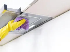 Gelbe Handschuhe wischen mit einem lila Tuch über die Dunstabzugshaube. Alu reinigen für strahlenden Glanz in der Küche.