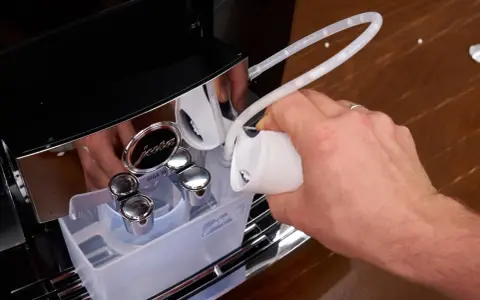 Hand gießt Flüssigkeit in einen Schlauch, um die Kaffeemaschine zu entkalken.