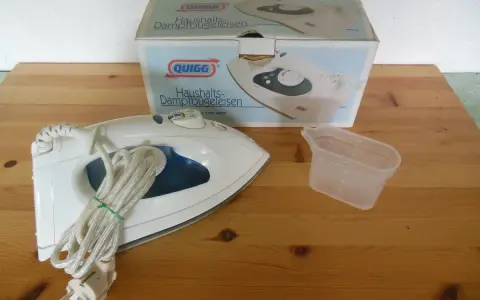 Ein Quigg Dampfbügeleisen mit Zubehör und Verpackung auf einem Holztisch.