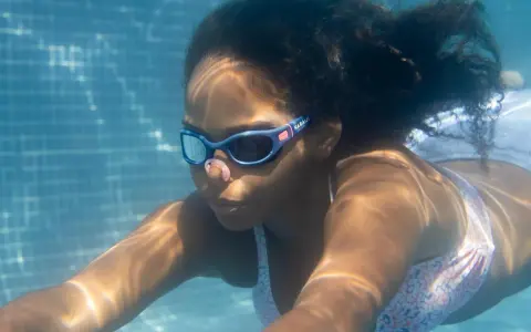 Ein Mädchen schwimmt unter Wasser. Ihre Schwimmbrille ist sauber und klar, damit sie alles sehen kann.