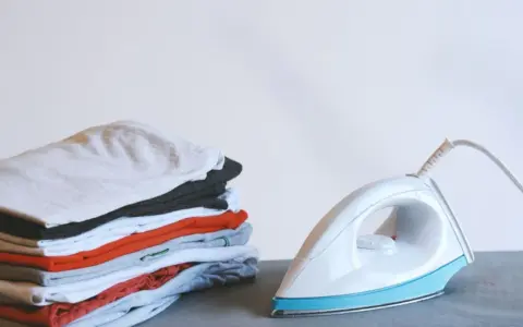 Ein Stapel bunter Kleidung neben einem weißen, easy home bügeleisen.