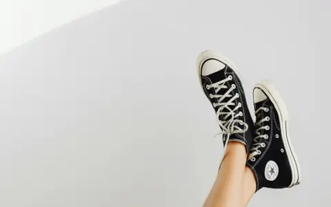 Beine mit schwarzen Chucks, die in der Luft baumeln. Zeit, die Lieblingsschuhe zu waschen!