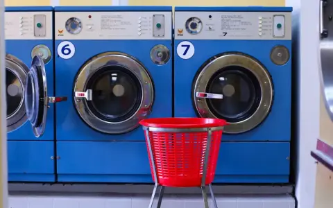 Reihen von blauen Waschmaschinen. Eine rote Wäschekorb steht davor. Ideal für die Waschmaschine reinigen 90 Grad.