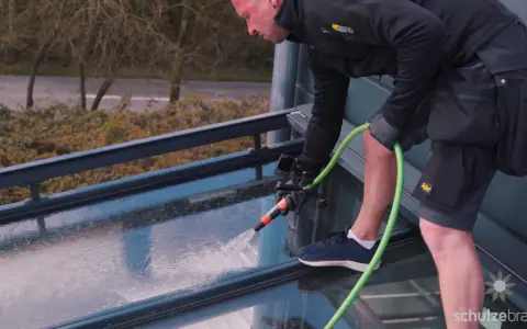 Mann reinigt mit Gartenschlauch das Glasdach von unten.