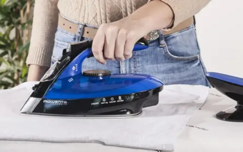 Eine Hand hält einen blauen, kabellosen Dampfbügeleisen über einem weißen Hemd.