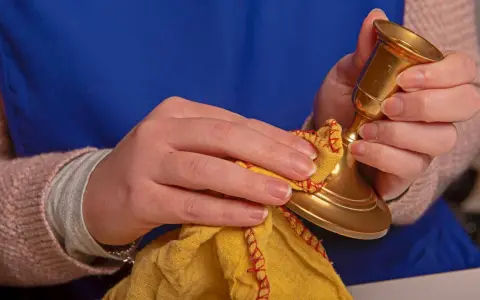 Hände polieren einen goldenen Kerzenständer mit einem gelben Tuch. Messing reinigen für neuen Glanz.
