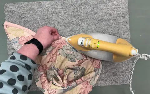 Ein kleines Bügeleisen zum Nähen glättet Stoff mit Blattmuster auf einer Filzmatte.
