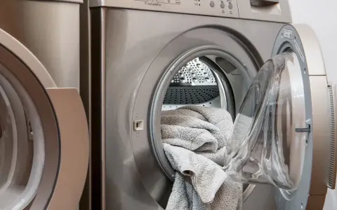 Waschmaschine mit offener Tür und grauen Handtüchern. Perfekt, um hartnäckige colaflecken entfernen zu lassen.