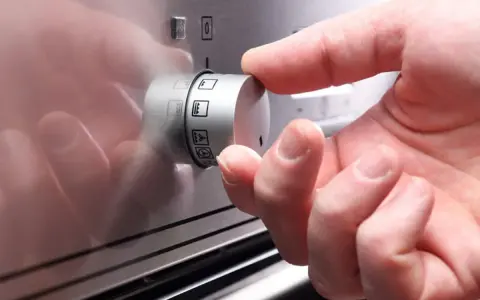 Hand dreht Regler mit Backofen Symbolen.