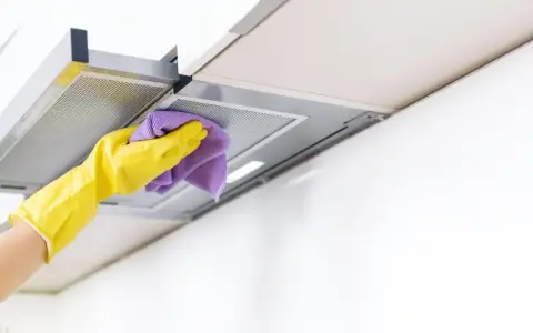 Gelbe Handschuhe wischen mit einem lila Tuch über die Dunstabzugshaube. Alu reinigen für strahlenden Glanz in der Küche.
