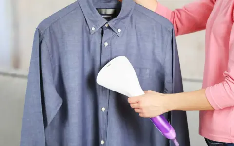 Dampfsteamer test: Eine Person glättet ein blaues Hemd mit einem Handdampfglätter.