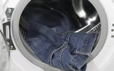 Eine blaue Jeans liegt in der Trommel einer Waschmaschine, bereit, um sie einlaufen zu lassen.