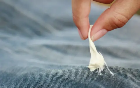 Finger zieht zähen Kaugummi aus Jeansstoff. Ein ärgerliches Malheur, das jeder kennt: Kaugummi aus Kleidung entfernen.