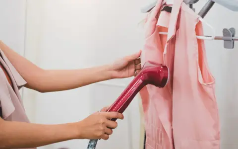 Eine Frau glättet mit einem Handdampfer ein rosa Kleidungsstück. Perfekt für die Vorbereitung auf die nächste steamer reise.