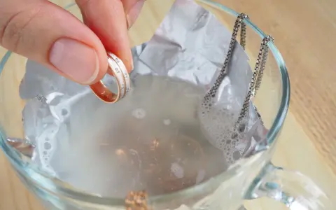 Ein Ring mit kleinen Steinen wird in eine Schüssel mit Wasser und Aluminiumfolie getaucht, um Schmuck zu reinigen.