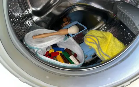 Bunte Lego-Steine in einem Wäschenetz, ein Spielzeugauto und ein gelbes Tuch in einer Waschmaschinentrommel.