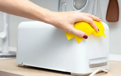 Eine Hand mit gelbem Tuch wischt über einen weißen Toaster. So einfach kann toaster reinigen sein.