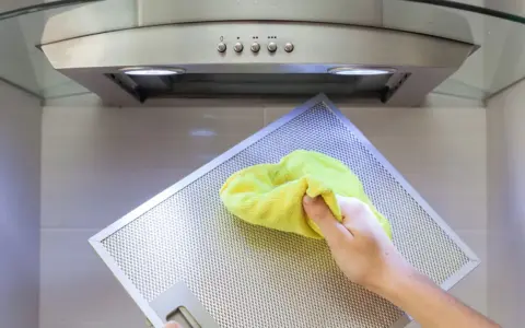 Hand reinigt Dunstabzugshaube mit gelbem Tuch.
