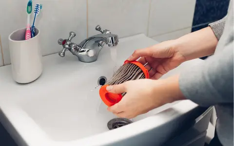 Hände reinigen einen staubigen Staubsaugerfilter unter fließendem Wasser im Waschbecken.