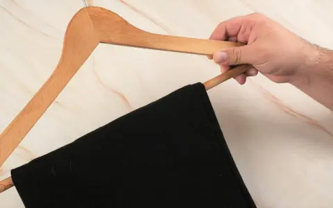 Hand hält einen Holz-Kleiderbügel mit einer schwarzen Anzughose. Zeit, die Anzughose zu waschen.
