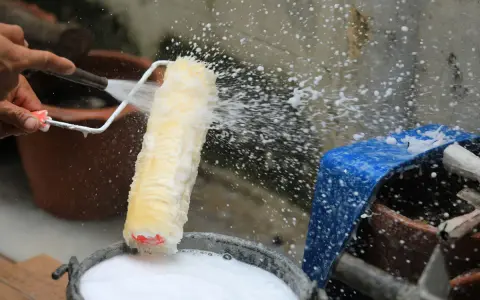 Eine Hand spritzt Wasser auf eine Malerrolle, um sie in einem Eimer mit Seifenwasser zu reinigen.