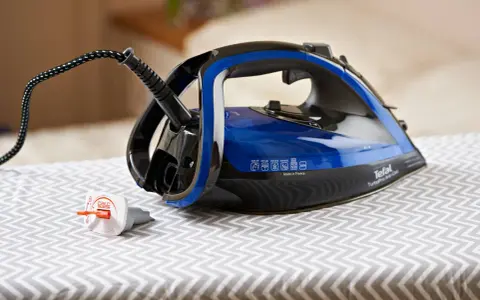 Ein Tefal Bügeleisen mit blauem Wassertank steht auf einem Bügelbrett. Der Stecker ist eingesteckt, aber das Bügeleisen scheint Wasser zu verlieren.
