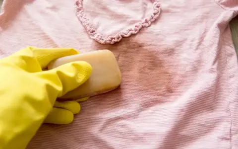 Gelbe Handschuhe halten Gallseife, um einen Fleck auf einem rosafarbenen gestreiften Shirt zu behandeln.