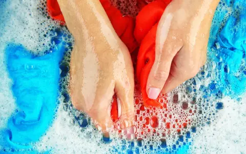 Hände waschen rote und blaue Sportsachen in schaumigem Wasser.
