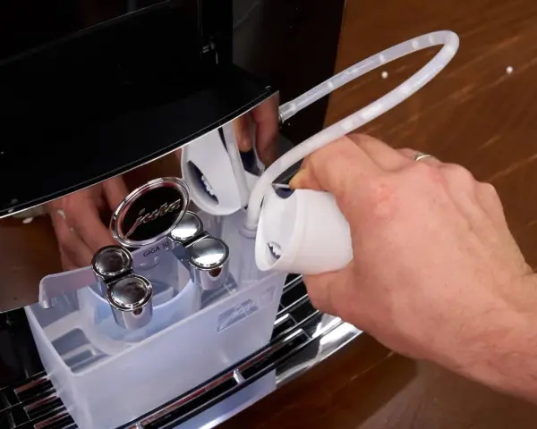 Hand gießt Flüssigkeit in einen Schlauch, um die Kaffeemaschine zu entkalken.
