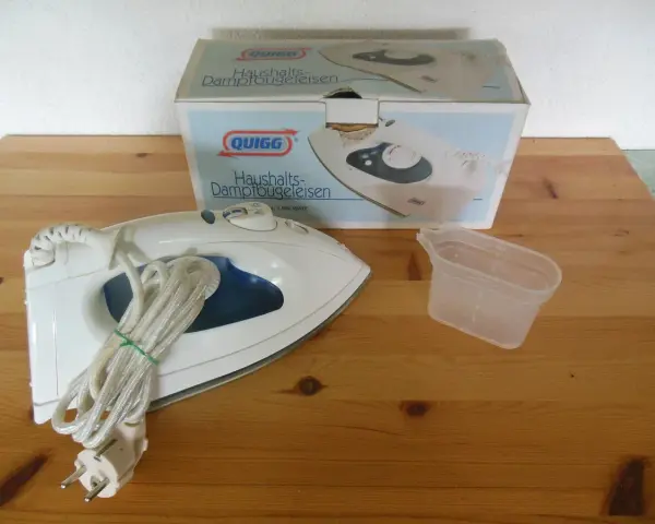 Ein Quigg Dampfbügeleisen mit Zubehör und Verpackung auf einem Holztisch.