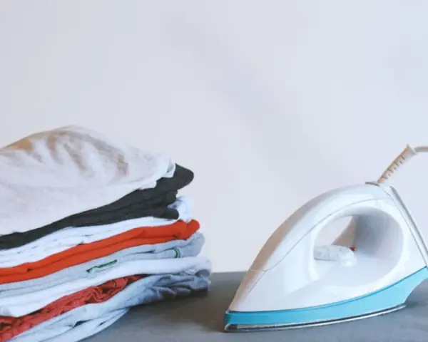Ein Stapel bunter Kleidung neben einem weißen, easy home bügeleisen.