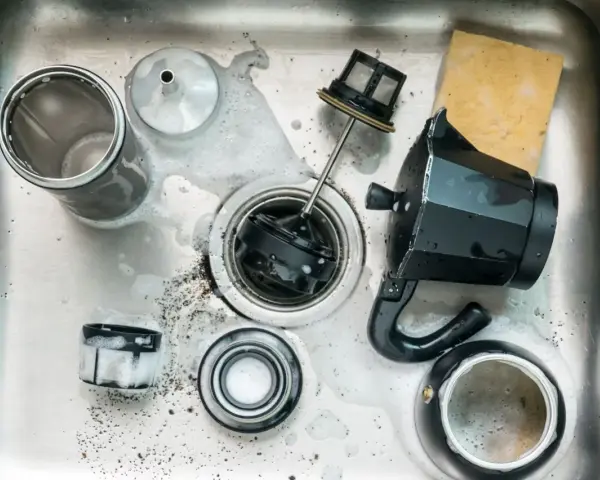 Zerlegte Edelstahl-Kaffeekanne mit Schaum und Kaffeesatz in der Spüle. Reinigung einer Espressokanne.