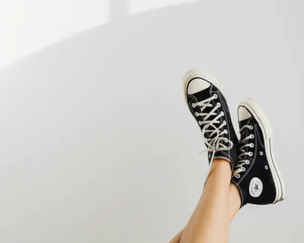 Beine mit schwarzen Chucks, die in der Luft baumeln. Zeit, die Lieblingsschuhe zu waschen!