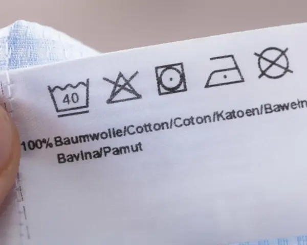 Pflegesymbol: Nicht im Trockner trocknen. Das Etikett zeigt auch Wasch- und Bügelsymbole für 100% Baumwolle.