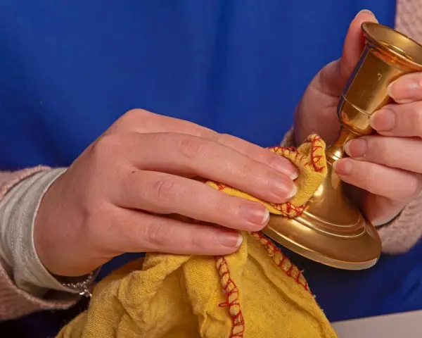 Hände polieren einen goldenen Kerzenständer mit einem gelben Tuch. Messing reinigen für neuen Glanz.