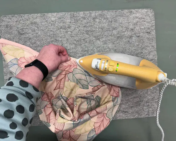Ein kleines Bügeleisen zum Nähen glättet Stoff mit Blattmuster auf einer Filzmatte.