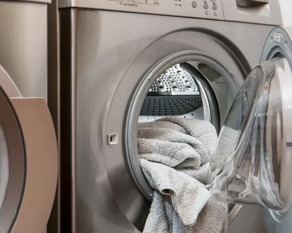 Waschmaschine mit offener Tür und grauen Handtüchern. Perfekt, um hartnäckige colaflecken entfernen zu lassen.