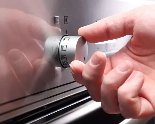 Hand dreht Regler mit Backofen Symbolen.