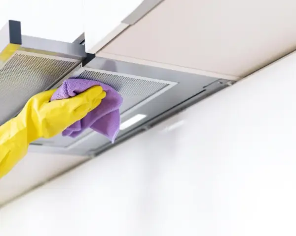 Gelbe Handschuhe wischen mit einem lila Tuch über die Dunstabzugshaube. Alu reinigen für strahlenden Glanz in der Küche.