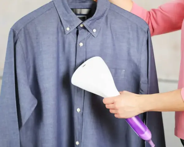 Dampfsteamer test: Eine Person glättet ein blaues Hemd mit einem Handdampfglätter.