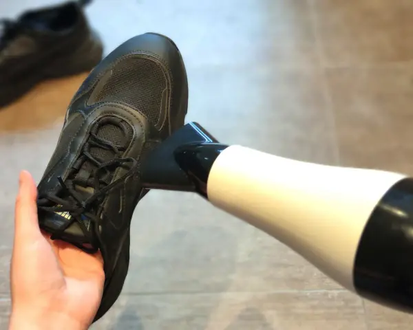 Schwarze Turnschuhe trocknen mit einem Föhn. Ein Paar nasse Schuhe wird mit einem Föhn getrocknet, um sie schnell wieder einsatzbereit zu machen.