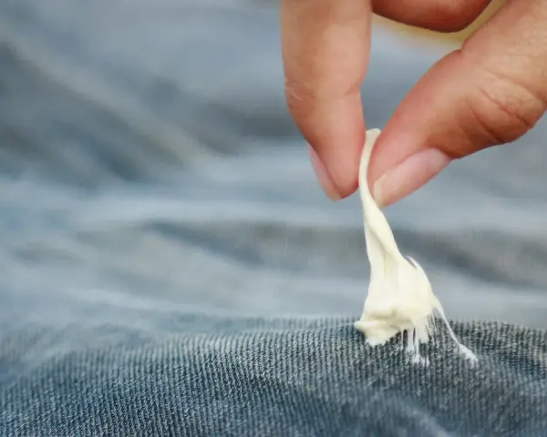 Finger zieht zähen Kaugummi aus Jeansstoff. Ein ärgerliches Malheur, das jeder kennt: Kaugummi aus Kleidung entfernen.