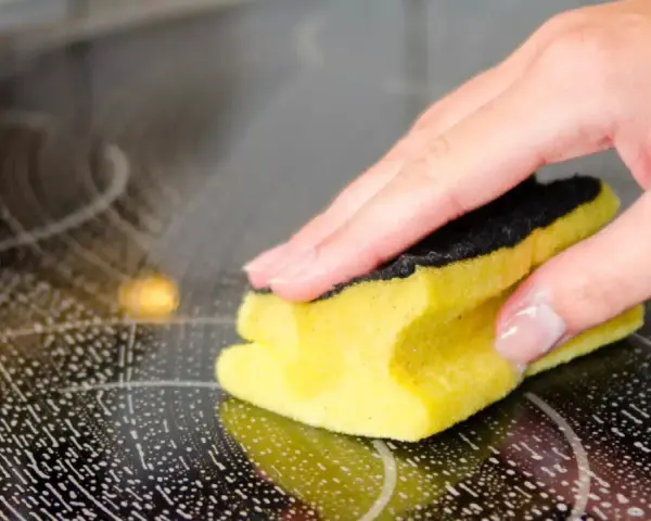 Hand reinigt mit Schwamm und Schaum das Ceranfeld.
