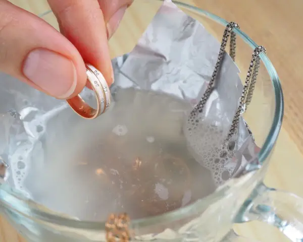 Ein Ring mit kleinen Steinen wird in eine Schüssel mit Wasser und Aluminiumfolie getaucht, um Schmuck zu reinigen.