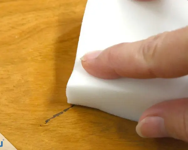 Mit einem weißen Schwamm wird ein Permanentmarker-Strich auf Holz entfernt.