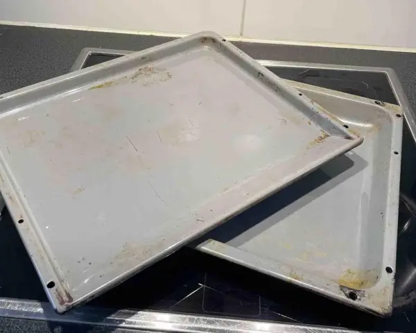 Zwei alte, graue Backbleche mit Gebrauchsspuren und Verfärbungen liegen übereinander auf einem Cerankochfeld. Zeit, das Backblech reinigen!