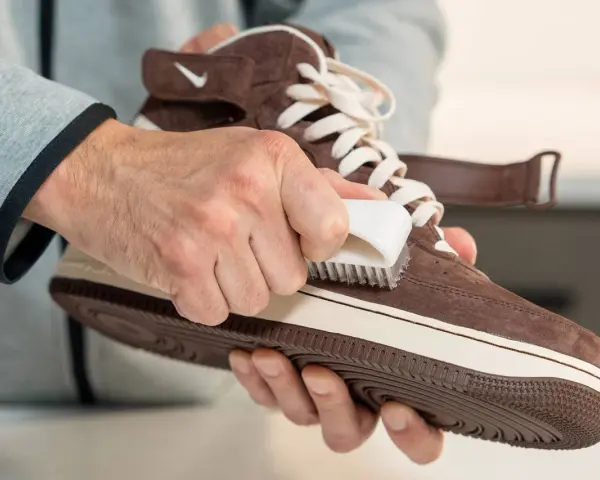 Hände reinigen braune Wildleder Schuhe mit einer Bürste. So werden die Lieblingssneaker wieder wie neu.