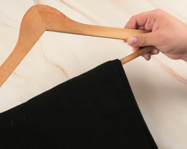 Hand hält einen Holz-Kleiderbügel mit einer schwarzen Anzughose. Zeit, die Anzughose zu waschen.