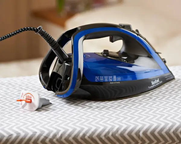 Ein Tefal Bügeleisen mit blauem Wassertank steht auf einem Bügelbrett. Der Stecker ist eingesteckt, aber das Bügeleisen scheint Wasser zu verlieren.