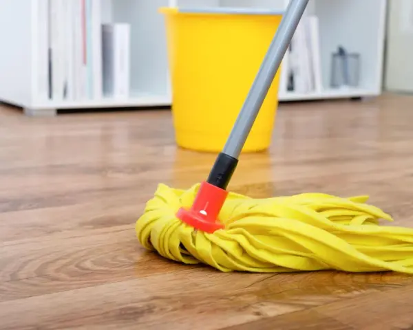 Gelber Wischmopp auf Laminatboden, bereit für die Reinigung mit Hausmitteln. Ein gelber Eimer steht im Hintergrund.